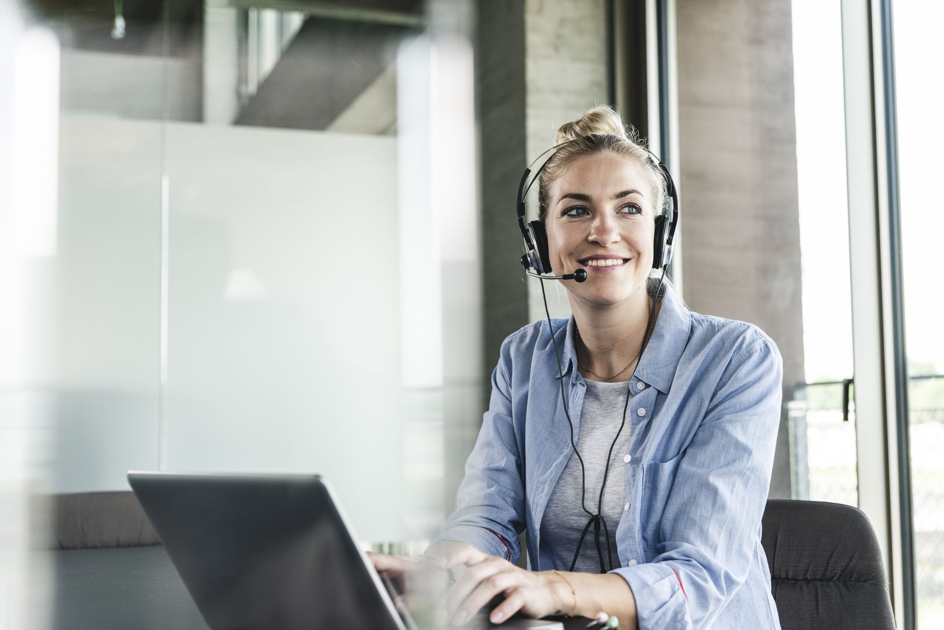 Woman with headset looks to the side while working on a laptop.