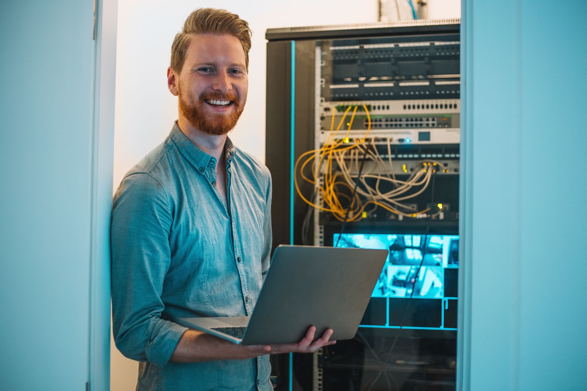 Man smiling with a laptop, standing in front of a wall in the interior.